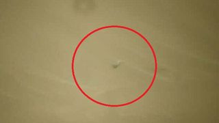 a broken helicopter blade lying on beige sand. the picture includes a circle drawn to show where the blade is