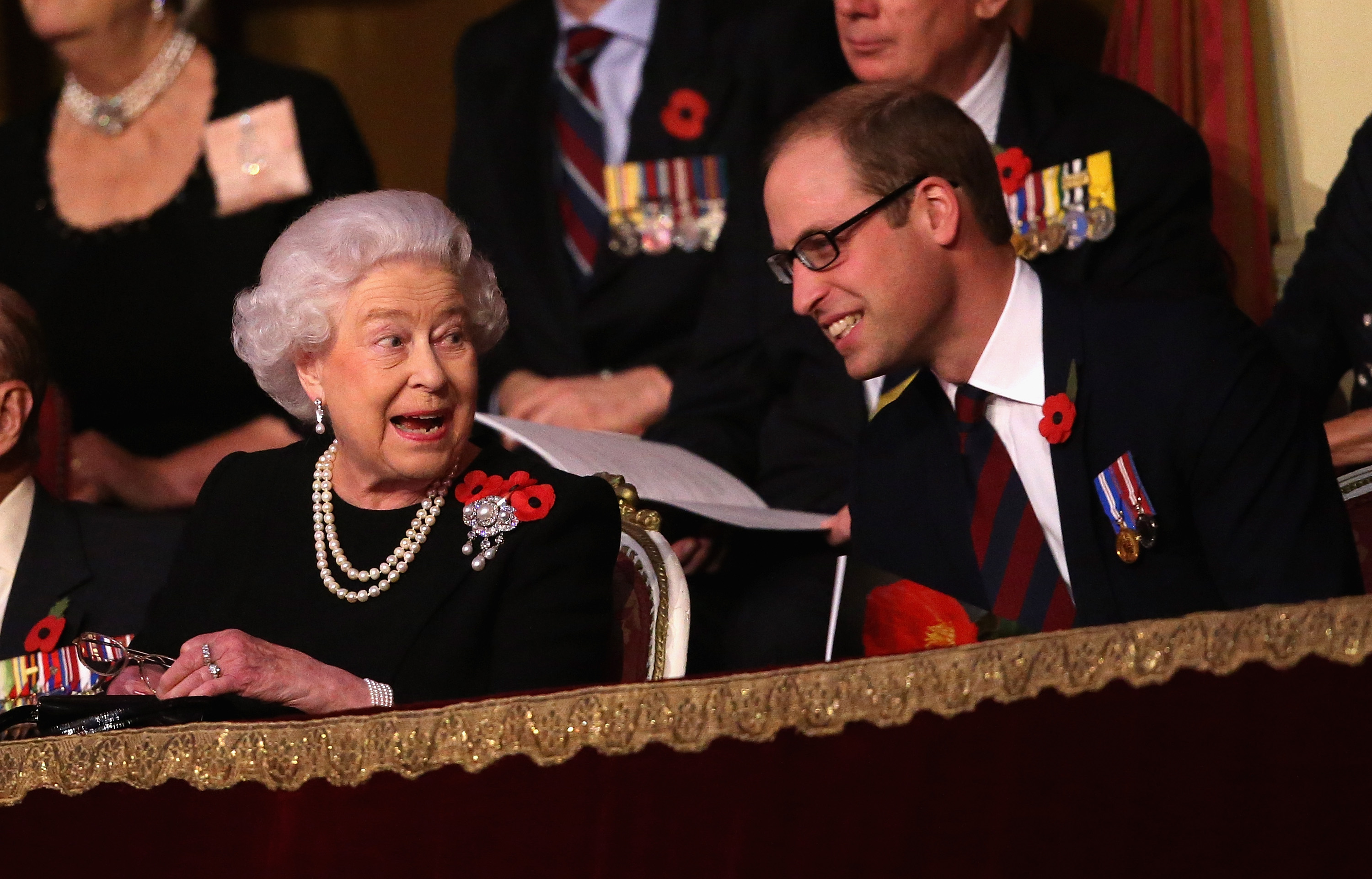 Prince William sitting next to Queen Elizabeth and smiling, both dressed in black, at Remembrance concert