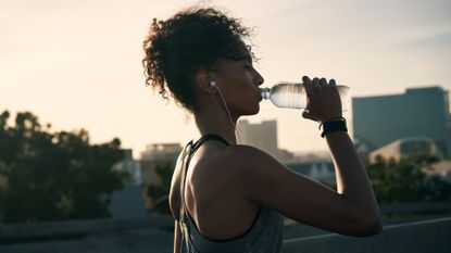 Attractive young woman wearing earphones and drinking water after her morning run in the city