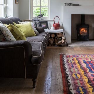 A cottagecore-style living room with a dark grey sofa with contrasting white piping and a colourful patterned rug