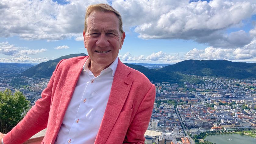 Michael Portillo in a pink jacket standing in front of a city in the distance 