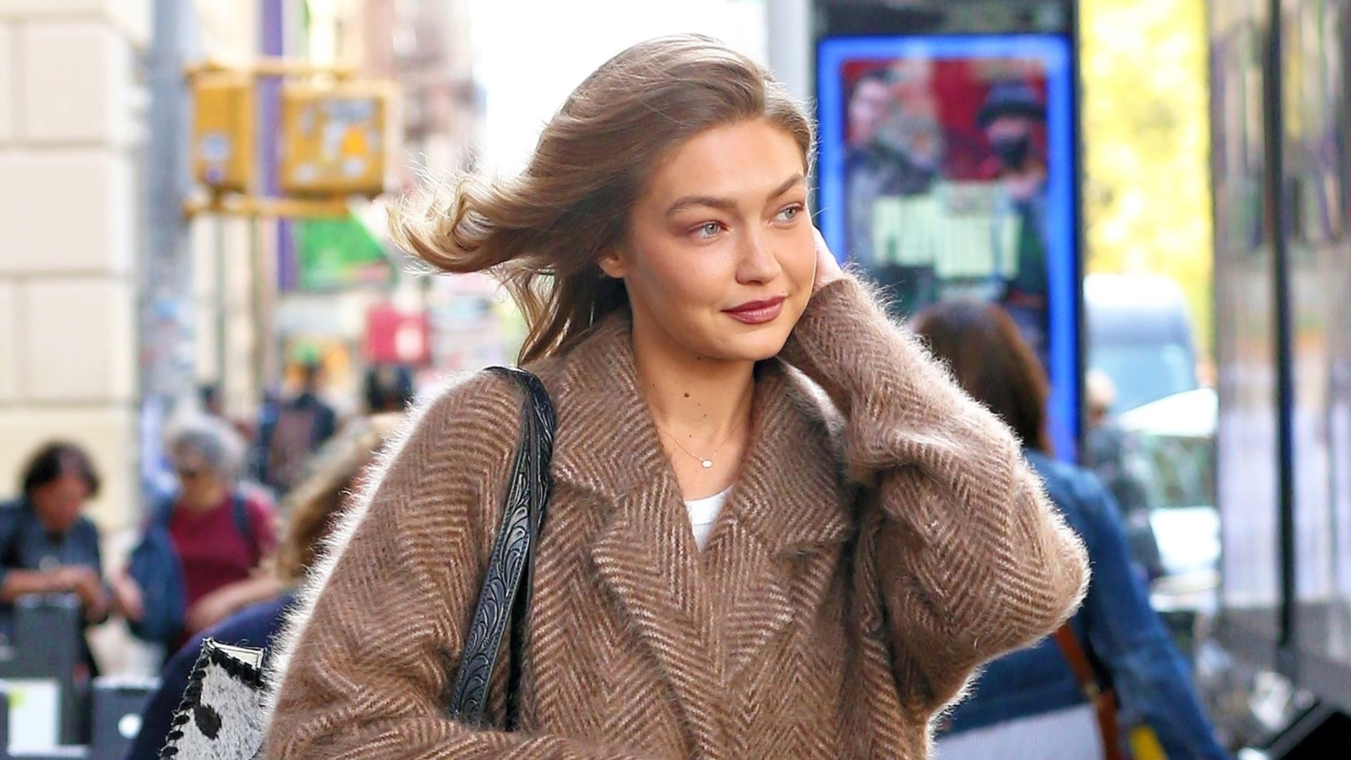 Gigi Hadid wearing a tan coat, baggy jeans, a cow-print bag, and Ugg boots