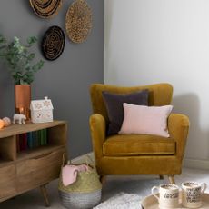 Velvet armchair in corner beside basket and woven plates on wall