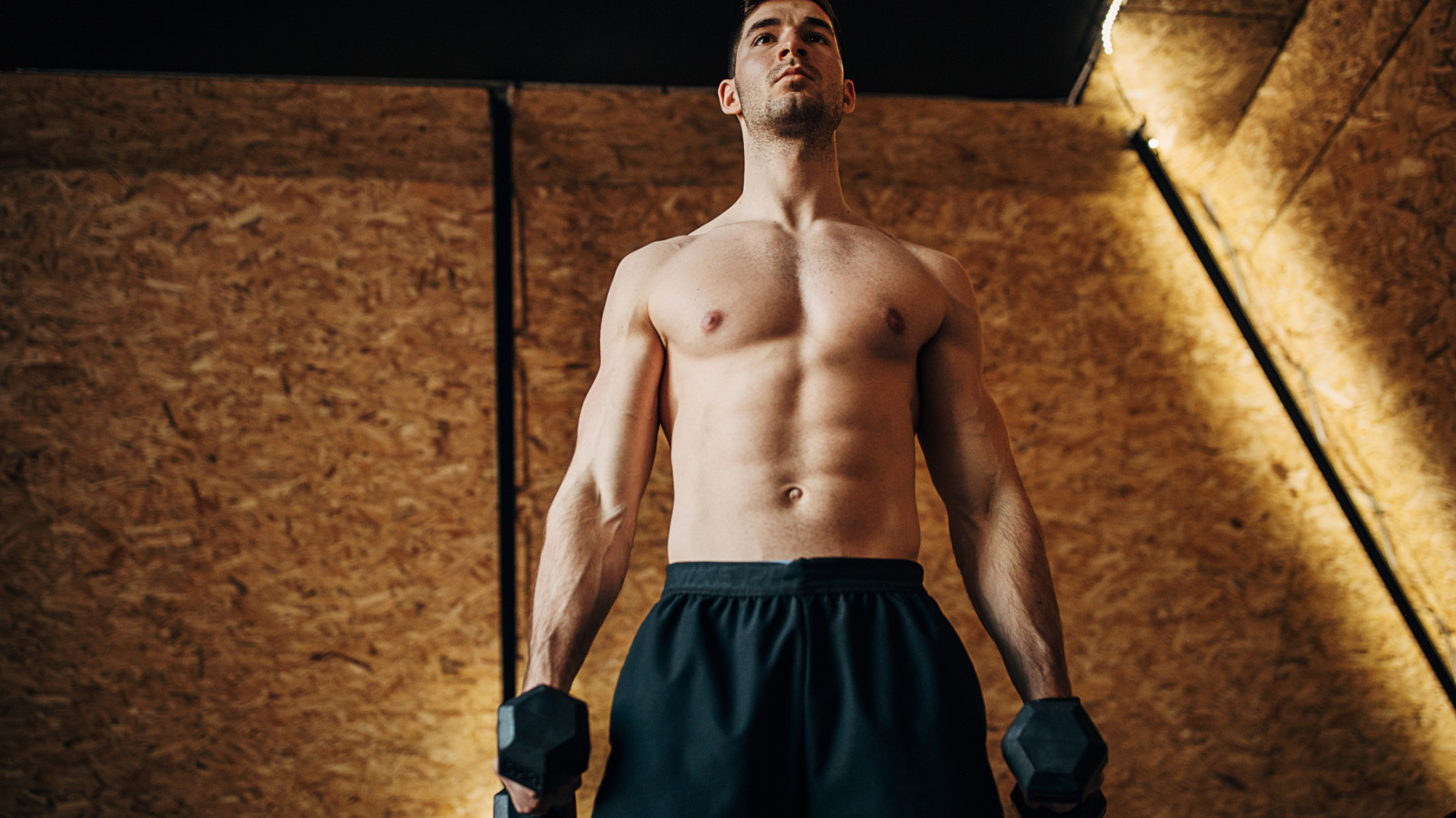 A topless man holding two dumbbells