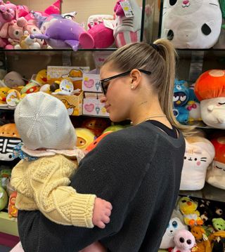 Sofia Richie Grainge wearing a black crewneck sweatshirt with a matching sports bra and black sunglasses while carrying her daughter at a toy store.