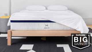A Helix Sleep Midnight mattress shown on a light wooden bed frame and dressed with a white comforter and pillows