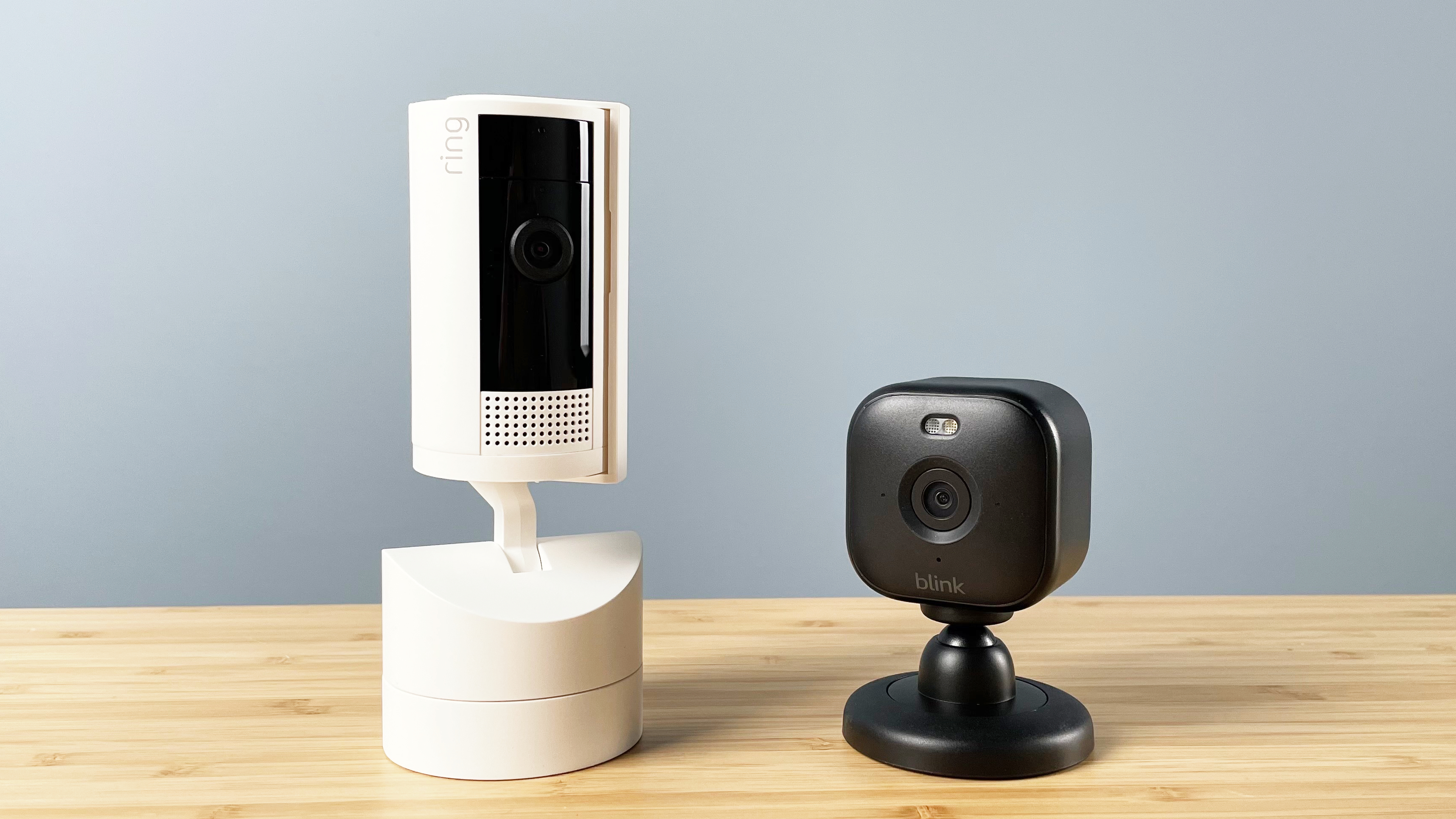 The Ring and Blink cameras stand side by side, both facing slightly off camera.