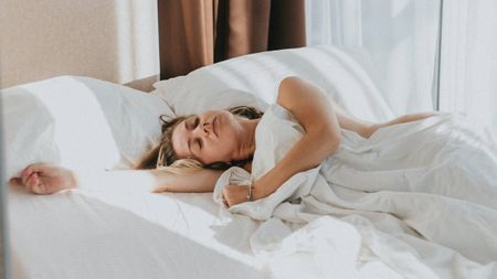 A woman asleep while lying in bed with white sheets, pillows and duvet