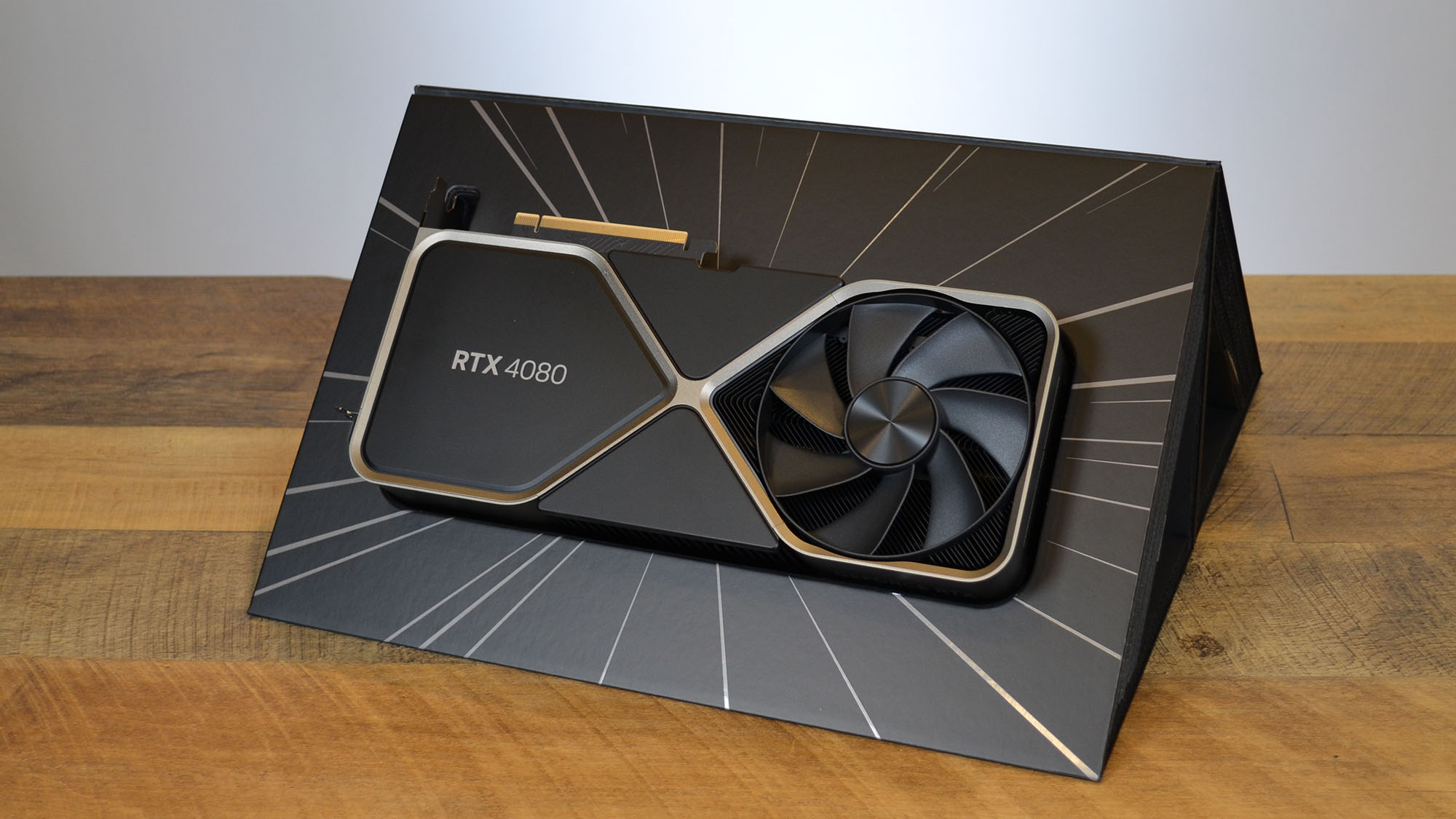 An Nvidia GeForce RTX 4080 on a wooden table in front of a white panel