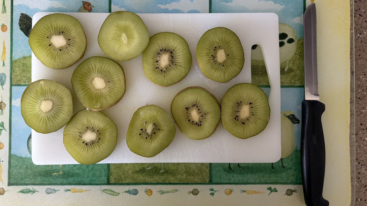 A close up of a chopped kiwi on a chopping board with a knife next to it