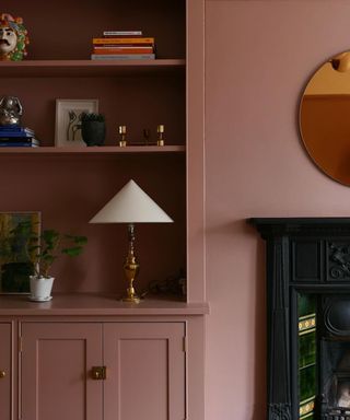 living room with dark pink walls and shelving, black fireplace and round mirror