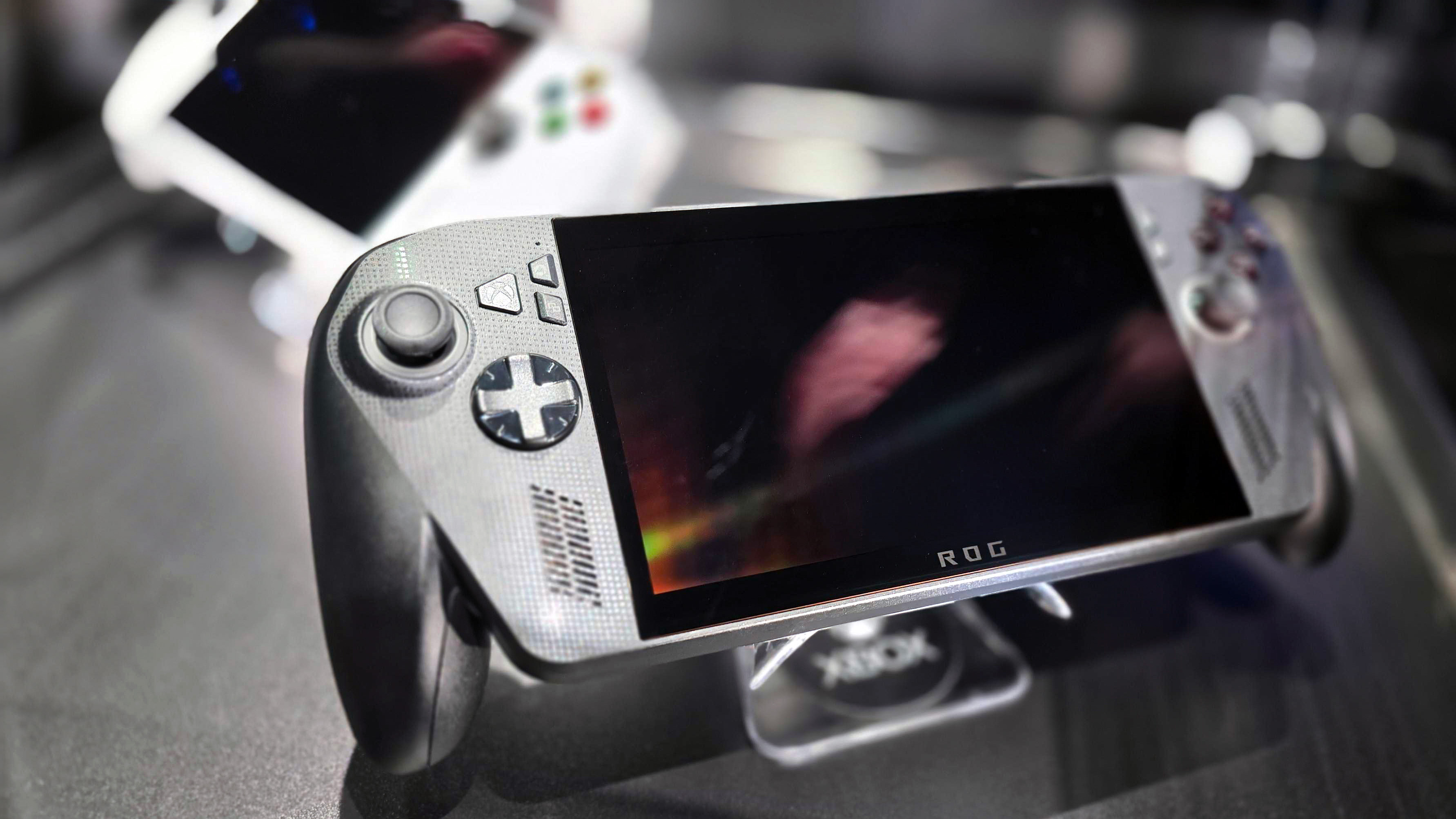 ASUS ROG Xbox Ally X (black) and ROG Xbox Ally (white) in a glass display case at Gamescom in August, 2025.
