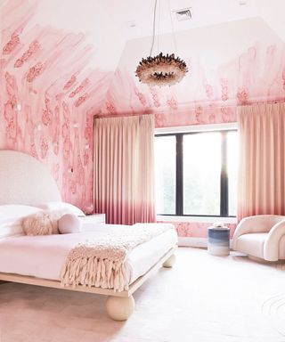 Beautiful pink bedroom with painted mural on walls that extends to the ceiling, cream carpet, pink curtains, unique, geometric upholstered cream bed, white and cream bedding, feathered style pendant light