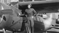 a black and white photo of Amelia Earhart standing in front of a plane