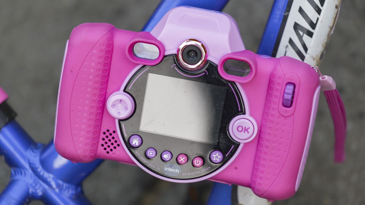 A pink V-Tech KidiZoom Duo camera resting on the blue and white frame of a kid's bike