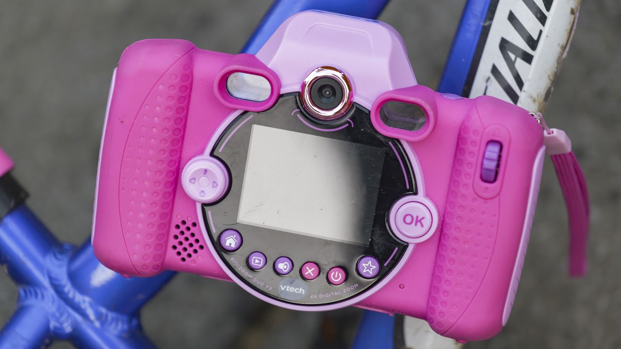 A pink V-Tech KidiZoom Duo camera resting on the blue and white frame of a kid's bike