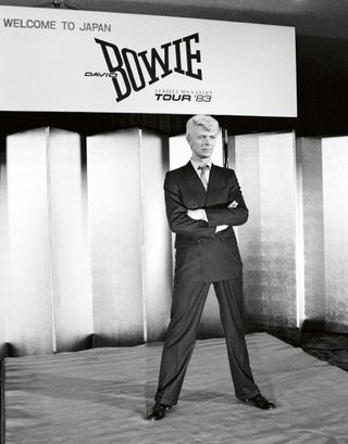 David Bowie standing on a stage wearing a striped suite in 1983.