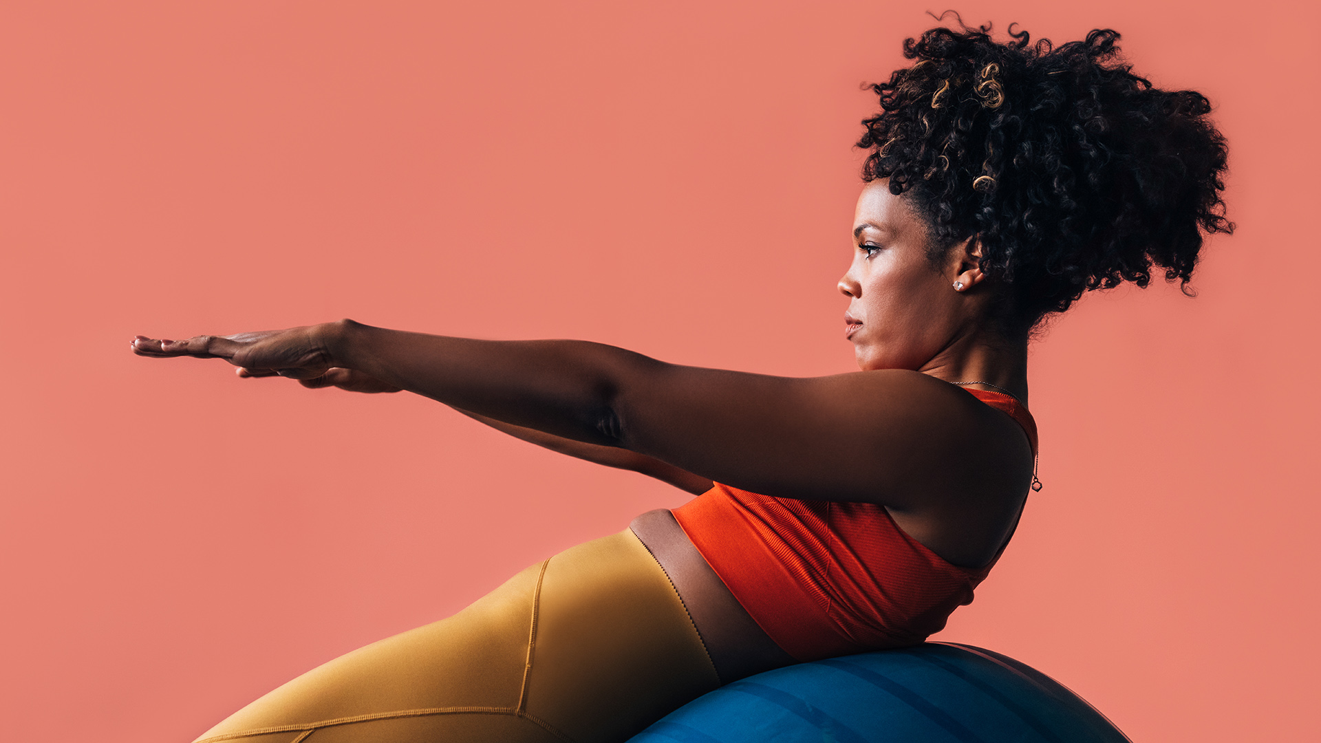 A side view of a focused Latin female athlete exercising. (studio shot, pink background, copy space)