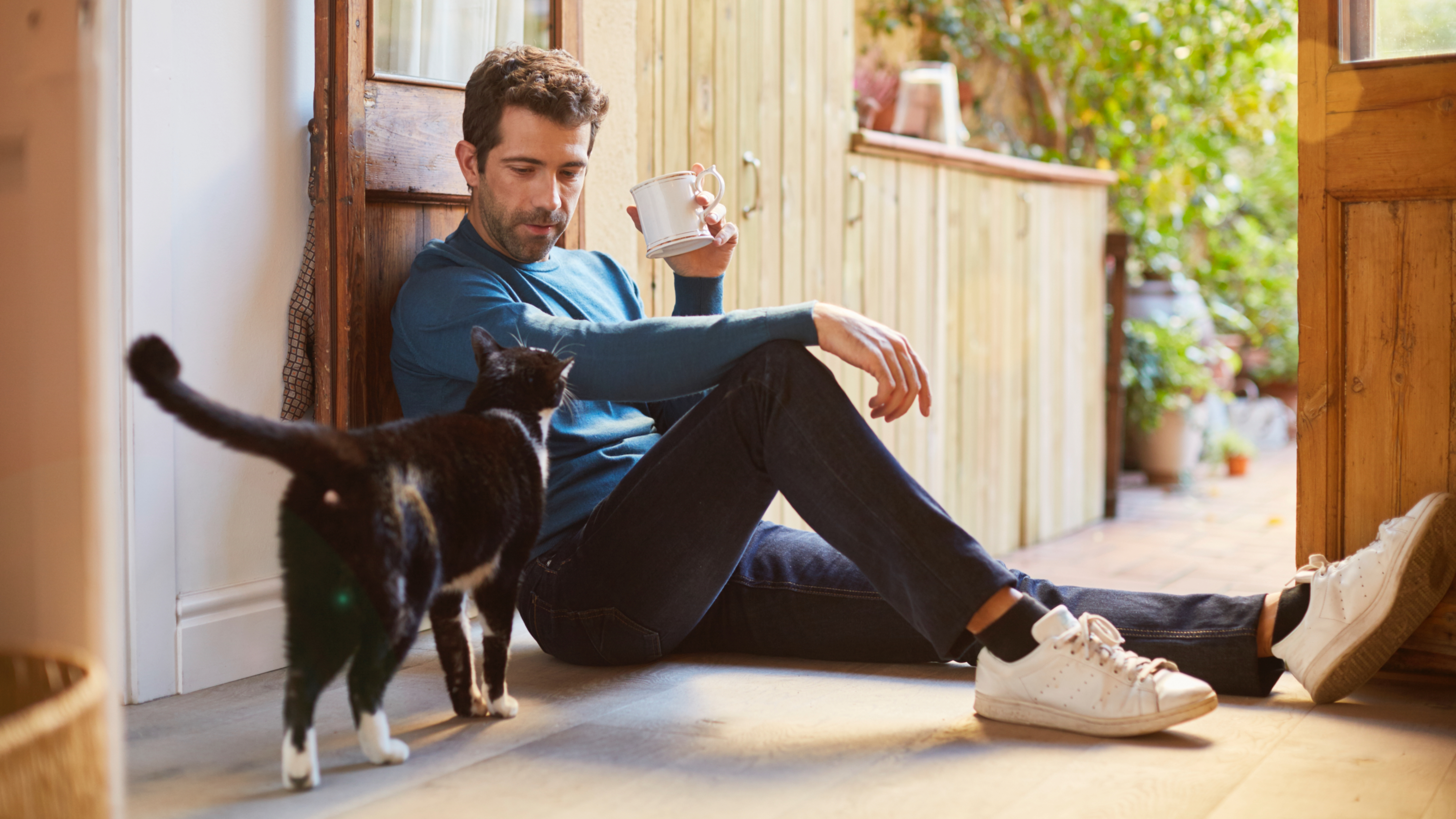 Man sitting on floor drinking coffee with cat