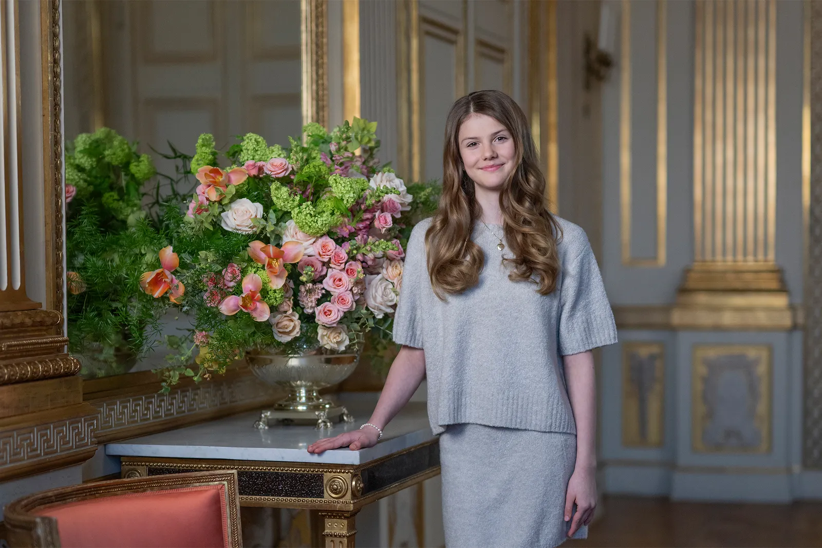 Princess Estelle wearing a gray skirt set standing next to a vase of flowers