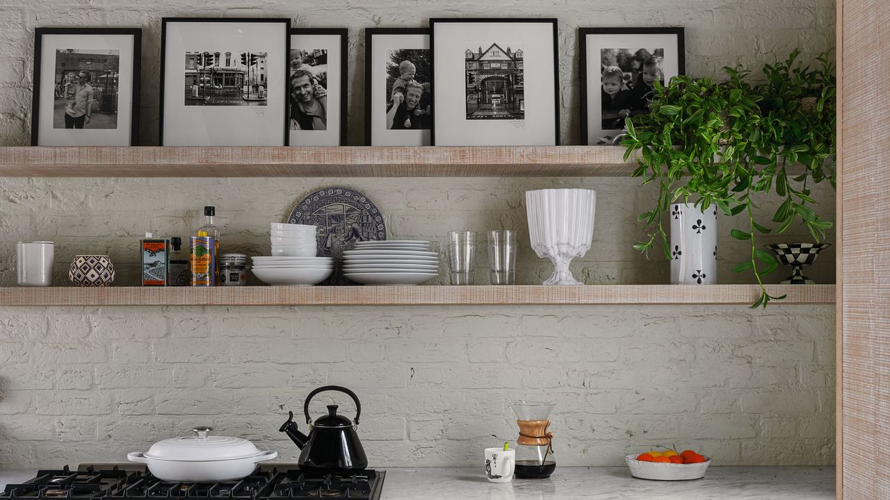 Modern kitchen range and fitted units with shelves and exposed painted brick wall and roof beams