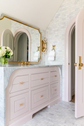 A bathroom with light pink and gold details