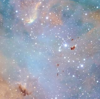A delicate pastel hue of blue and pink washes over this image stars, like a watercolor painting. There are dark brown fragments spread across the image, these are Bok globules.