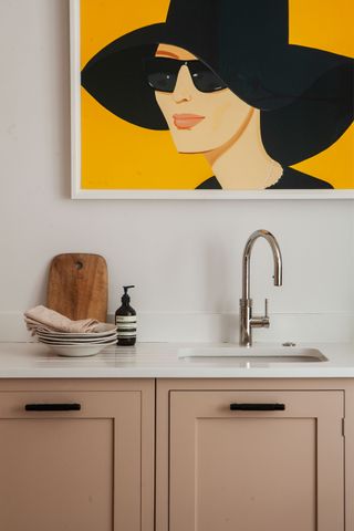 Kitchen color ideas featuring plaster pink painted cabinets, white walls and bright yellow artwork.