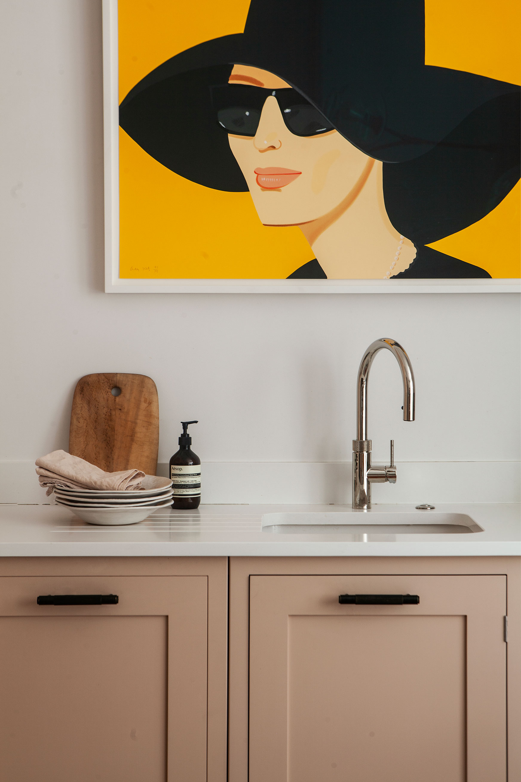 Kitchen color ideas featuring plaster pink painted cabinets, white walls and bright yellow artwork.