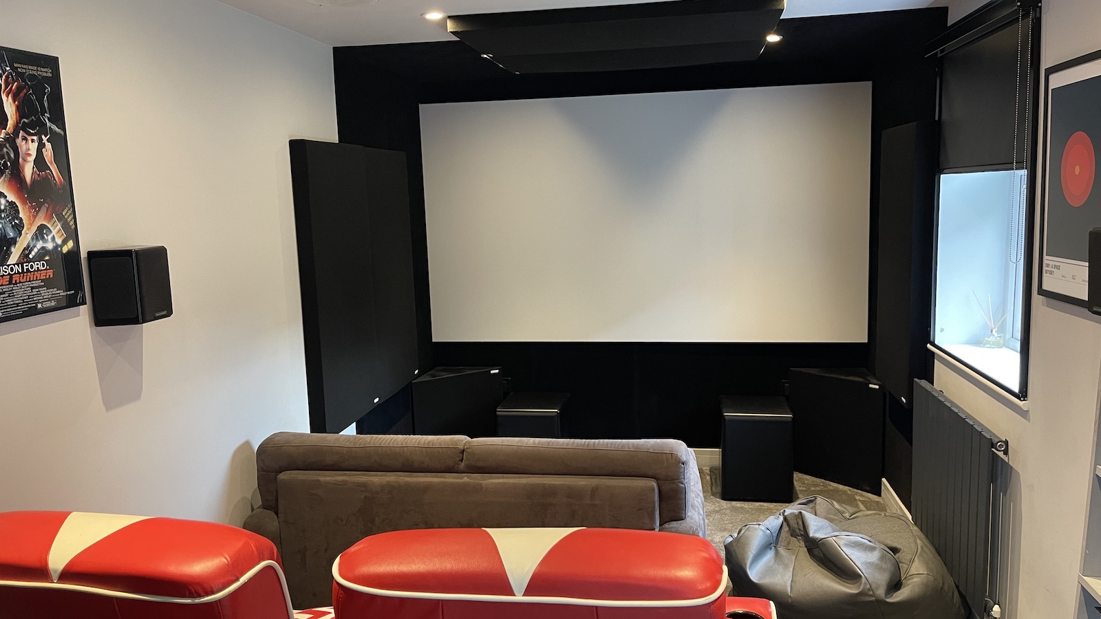 A photograph of a dedicated home cinema room featuring bright red seating