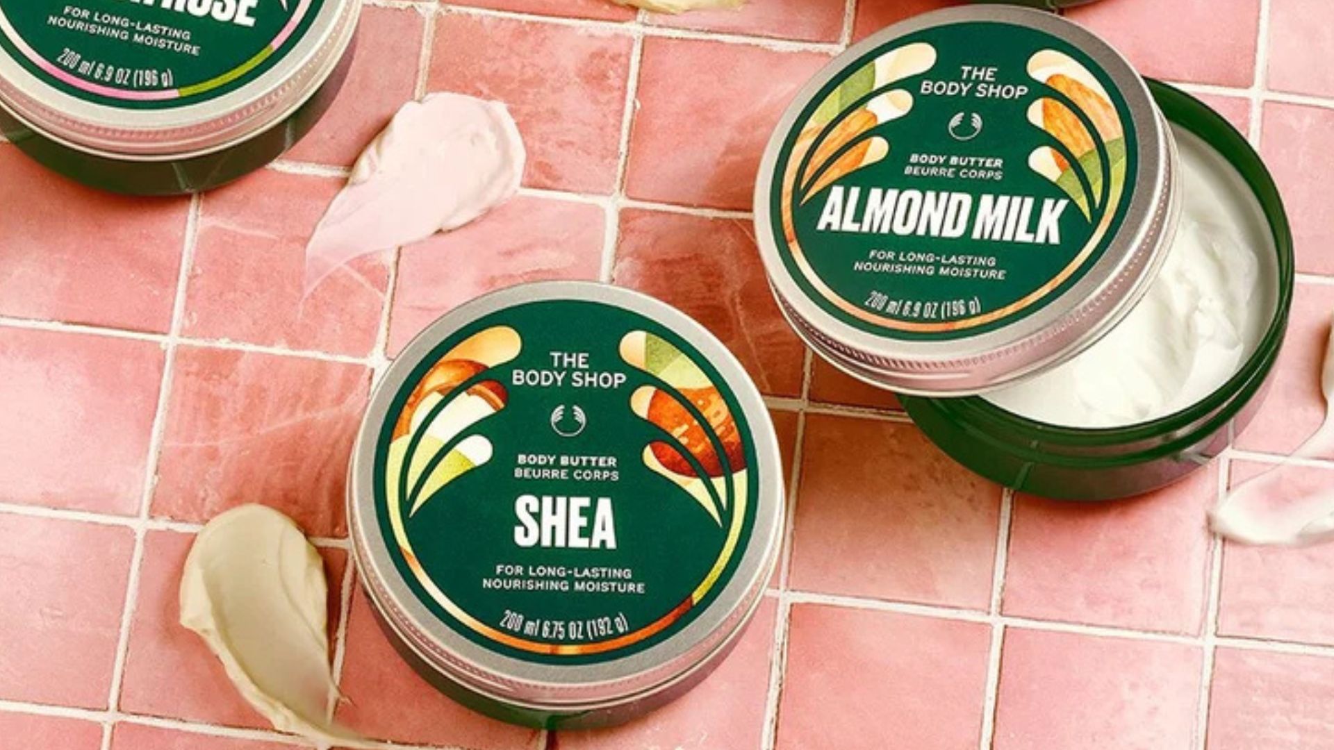 three body butters pictured on a pink tiled backdrop with smears of product