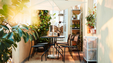 IKEA's space-saving $35 TVET&Ouml; umbrella shading a charming black iron patio dining set atop of a small patio accented with potted plants
