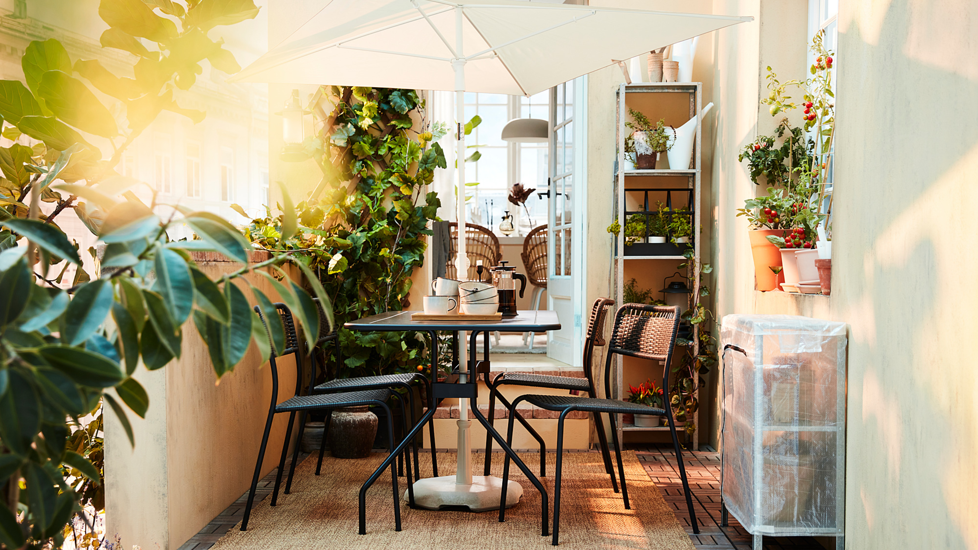 IKEA's space-saving $35 TVET&Ouml; umbrella shading a charming black iron patio dining set atop of a small patio accented with potted plants