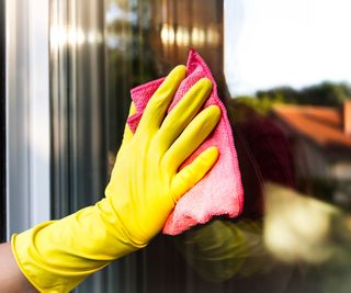 Someone wearing a cleaning glove wiping a window with a pink cloth