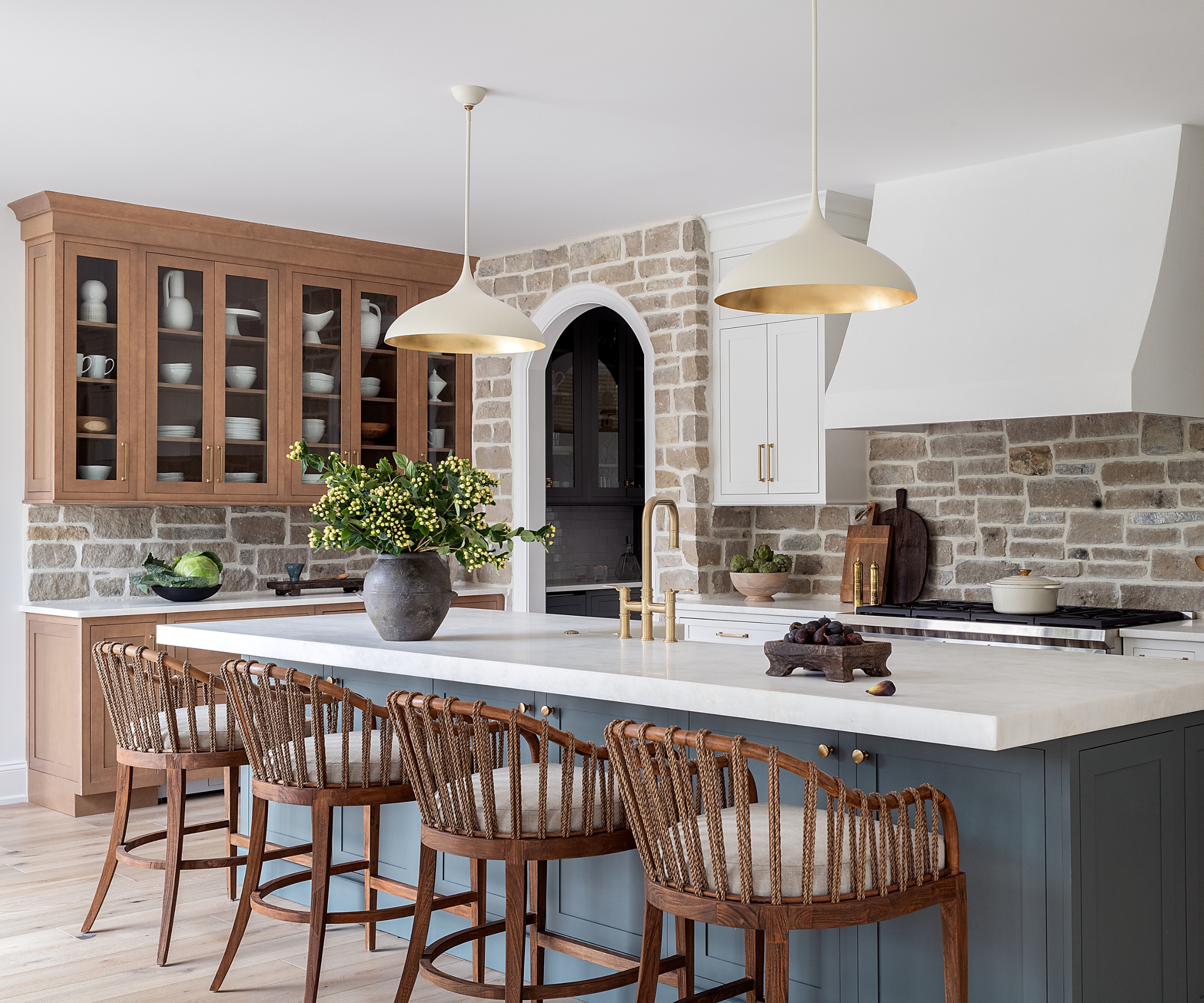 an L-shaped kitchen with island with wooden perimeter cabinets, a blue island, and exposed stone walls