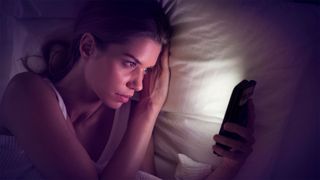 A woman looks at a smartphone in bed