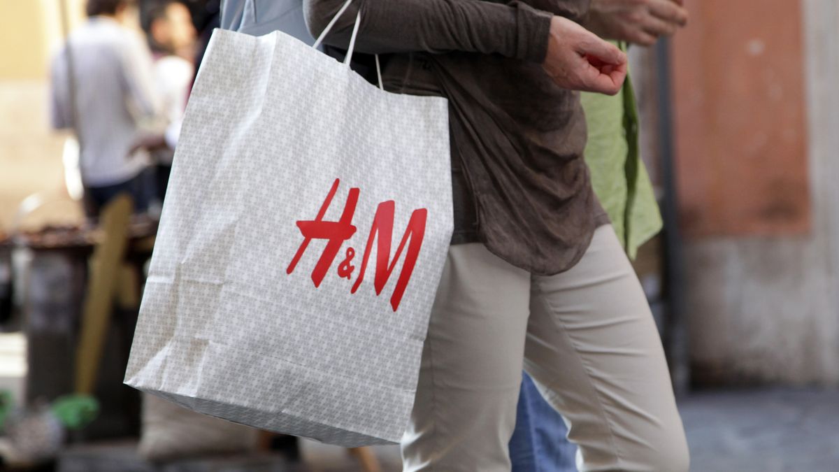 A shopper holding an H&amp;amp;M bag full of items in a busy high street 