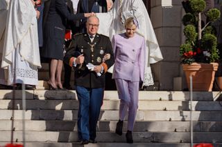 Princess Charlene wears a lilac pink pant suit and links arms with husband Prince Albert II of Monaco