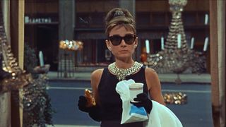 Audrey Hepburn holds a coffee and a croissant in sunglasses in front of Tiffany's