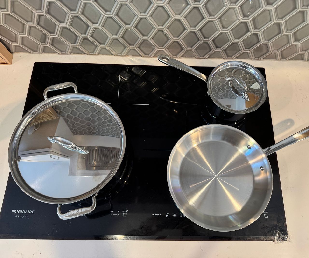 A set of three stainless steel drying pans on a black induction stove, viewed from above.