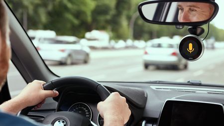 A man driving along a road with the Chris digital assistant screen attached to his windscreen – one of the best car accessories