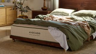 Natural sunlight hits the earth-toned organic bedding that covers the Avocado Extra Firm Mattress in a neutral bedroom.