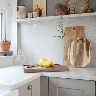 White kitchen worktop with cutting board and kitchen knife, white kitchen shelving