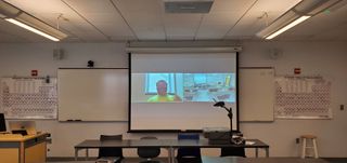 In this university classroom application by CCS, the right side of the laptop shows the front of the classroom as captured by the 1 Beyond AutoTracker camera on the back wall. Mounted on the wall next to the 1 Beyond camera is a Panasonic TH-65EQ1U reference monitor.