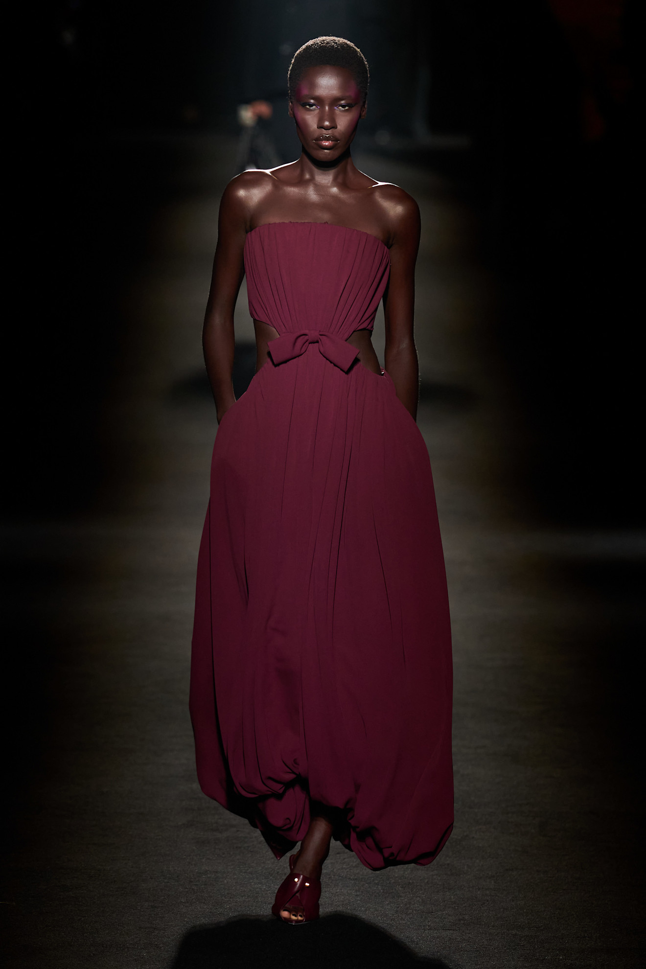 A model walking in the F/W 26 Balenciaga show wearing a burgundy strapless gown with cutouts.