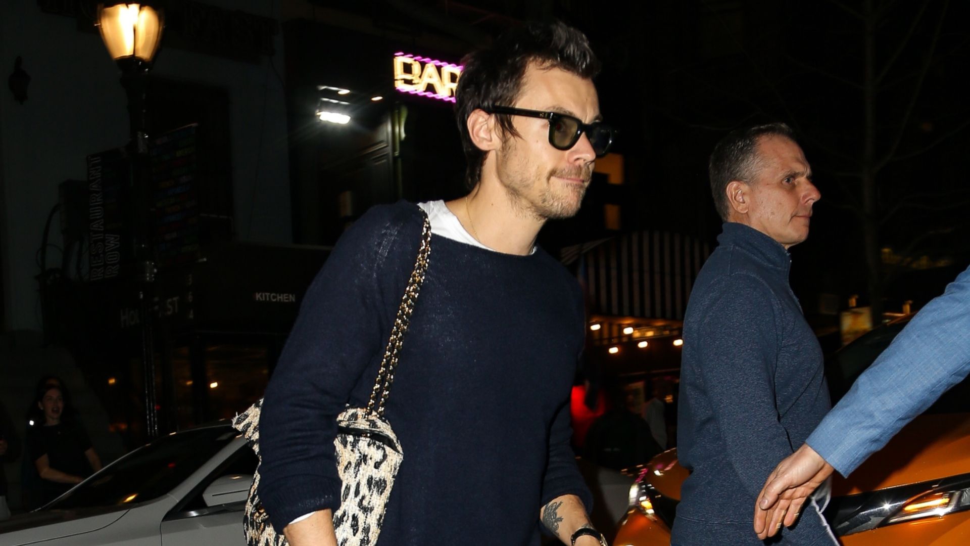 Harry Styles steps out wearing straight-leg jeans with a navy jumper, loafers and a leopard print Chanel bag.