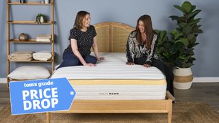 Two women sit on the Helix Dawn Mattress in a bedroom, a Tom's Guide price drop deals graphic (left)