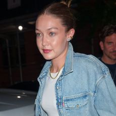 Gigi Hadid wearing a denim jacket, metallic track pants, and mesh flats