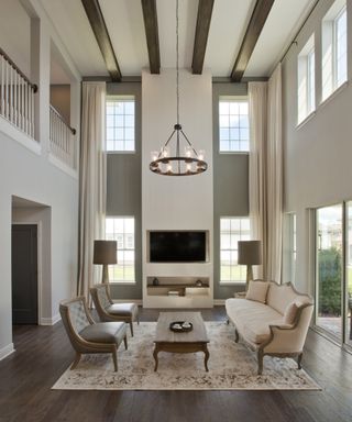 Neutral living room with double height ceiling, area rug, sofa and facing chairs, coffee table, beamed ceiling and chandelier