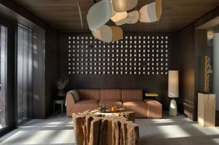 A playfully decorated ski hotel lounge features organic colors, a large, brown sofa with soft lines, a coffee table carved from a tree, and a wall installation made of small ceramic pieces.